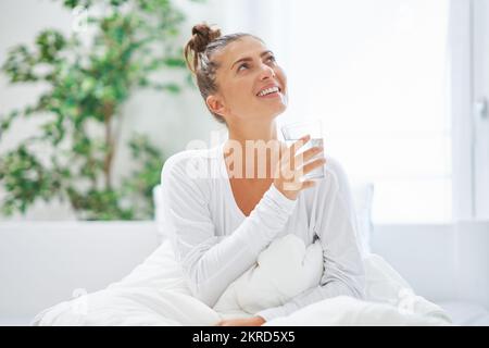 Young brunet woman relaxing on bed with water Stock Photo