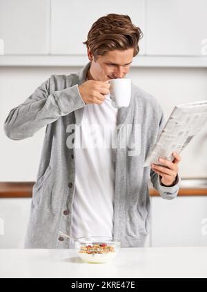 My morning ritual...A handsome young man drinking a hot beverage and reading a newspaper. Stock Photo