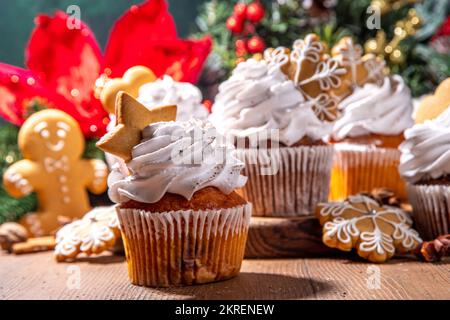 Christmas gingerbread cupcakes. Sweet chocolate and white muffin cupcakes with whipped cream, winter spices and gingerbread cookies decor, on wooden c Stock Photo