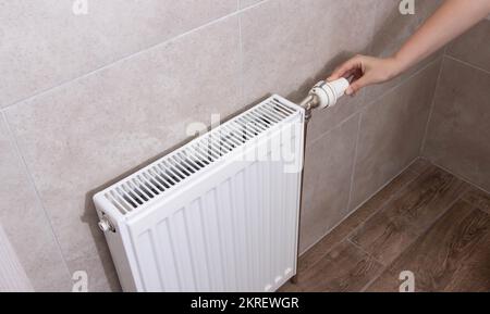 A woman regulates the gas heating in the room in order to save gas energy, taking into account the sanctions. Comfortable heating in the house. Stock Photo