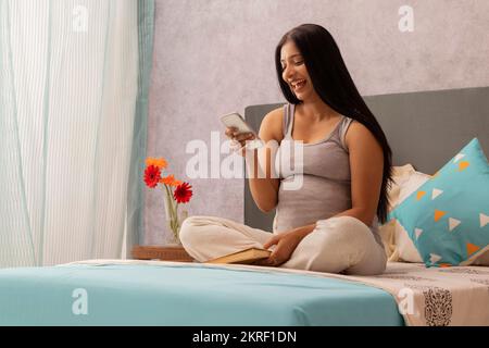 Pregnant woman using mobile phone while sitting on bed Stock Photo