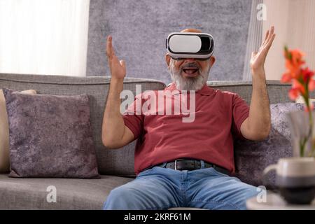 Portrait of an excited senior man experiencing virtual reality eyeglasses headset at home in the living room Stock Photo
