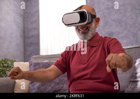 Portrait of an excited senior man experiencing virtual reality eyeglasses headset at home in the living room Stock Photo