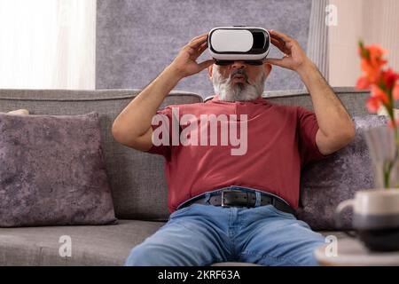 Portrait of an excited senior man experiencing virtual reality eyeglasses headset at home in the living room Stock Photo