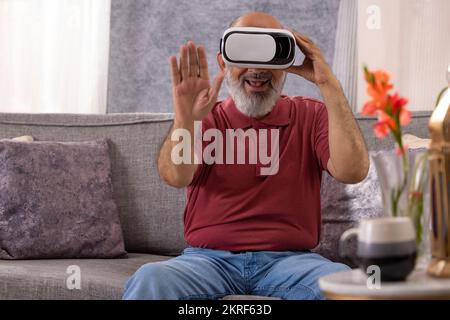 Portrait of an excited senior man experiencing virtual reality eyeglasses headset at home in the living room Stock Photo