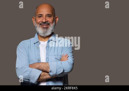 Portrait of cheerful senior man with arm crossed against grey background Stock Photo