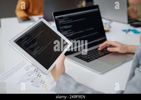 Close-up of programmer working on computer and digital tablet, he writing computer codes at table at IT office Stock Photo