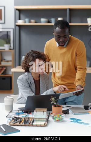 Two young colleagues discussing online presentation on digital tablet in team at office Stock Photo