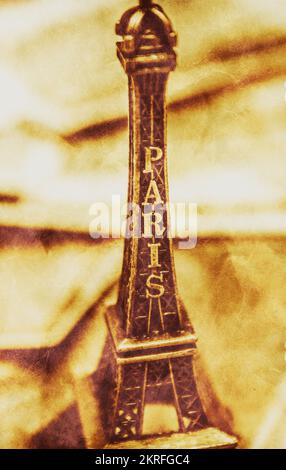 Creative antique still life photo on a miniature Eiffel Tower layered with sepia toned paper texture. Paris Decor Stock Photo