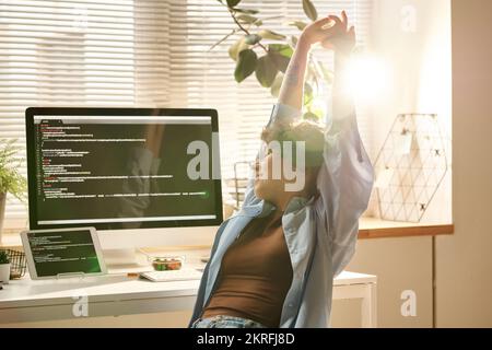 Young IT developer relaxing after work on computer, she sitting at her workplace and doing stretching exercises Stock Photo