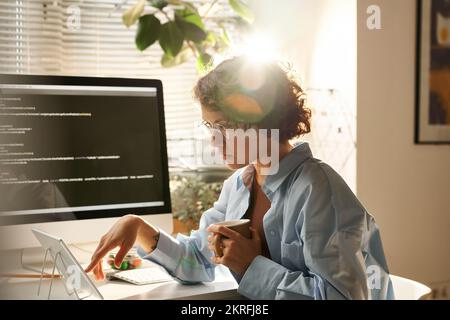 Young IT programmer using tablet pc to work with computer program while working at her workplace at office Stock Photo