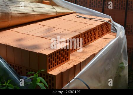 Stacks of packed in waterproof film bricks outdoor. Large brick stack protected from rain on the house construction site. Stock Photo