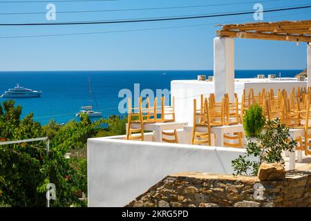 Ios, Greece - September 15, 2022 : View of a closed restaurants terrace with chairs, tables and the Mylopotas beach in the background in Ios Greece Stock Photo