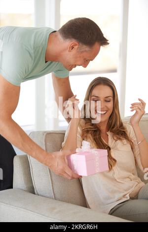 I think its something youll really like. a handsome man surprising his wife with a gift. Stock Photo