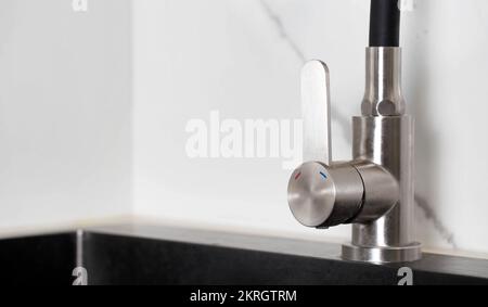 High-quality kitchen faucet for regulating cold and hot water against the backdrop of white porcelain stoneware tiles. Stock Photo