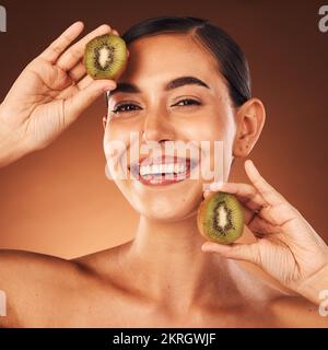 Cosmetics, skincare and young woman with kiwi, natural beauty or healthy with brown studio background. Portrait, makeup or healthy girl with fruit Stock Photo