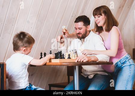 Pregnant mother watches as dad and son play chess at the table Stock Photo
