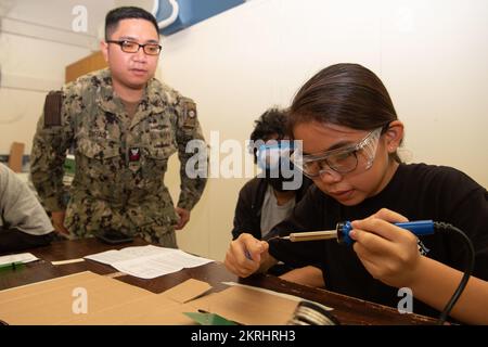 HONOLULU, Hawaii (Nov. 17, 2022) Cryptologic Technician (Technical) 1st Class Dylan Diras, assigned to Commander, U.S. Pacific Fleet, assists a student from Ke'elikolani Middle School’s STEM program use a soldering iron in order to build a fully functioning Remotely Operated Vehicle for the annual International SeaPerch Challenge. Sailors and other volunteers help students learn how to use tools safely and employ the engineering design process at an early age during the after-school STEM program. Community,Volunteer,stem, Stock Photo