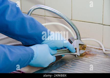 The plumber unscrews the old rusty faucet in the kitchen wrench. The master works in rubber protective gloves. Stock Photo