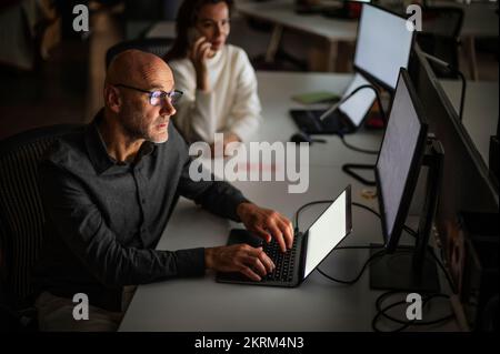 Shot of a businessman looking thoughtfully while sitting at his desk in the office in late evening. Confident businesswoman sitting next to him and wo Stock Photo