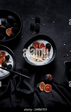 From above of appetizing healthy breakfast consisting of yogurt fresh figs and blackberries sprinkled with seeds and nuts placed on black table Stock Photo