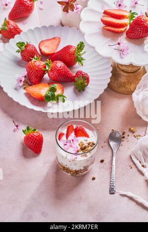 From above of glass of delicious yogurt with granola placed on table near plates of fresh ripe strawberries served on table in kitchen Stock Photo