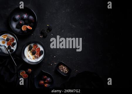 From above of appetizing healthy breakfast consisting of yogurt fresh figs and blackberries sprinkled with seeds and nuts placed on black table Stock Photo