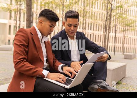 Focused Hispanic businessmen in classy outfits with documentation using laptop while working remotely on project together Stock Photo