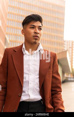 Low angle of serious Hispanic man in elegant suit standing on city street looking away Stock Photo