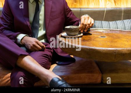Stylish cropped unrecognizable African American male freelancer in suit and tie drinking coffee while sitting in cafe Stock Photo