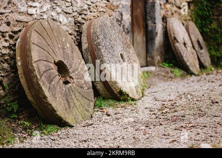 Shabby millstones placed near stone wall of aged hut in daytime in village Stock Photo