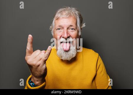 Portrait of elderly man in colorful sweater while showing horn sign looking at camera Stock Photo