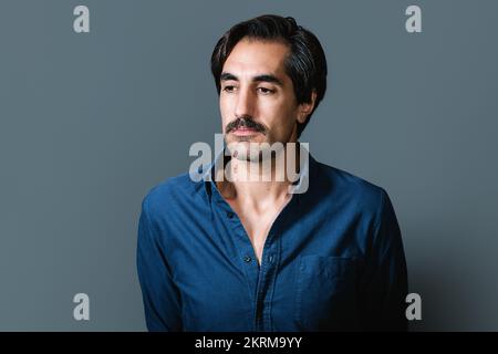 Confident young male in blue shirt on gray background and looking away Stock Photo