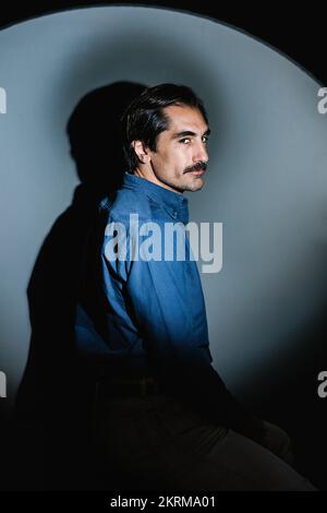 Side view of confident adult man in blue shirt looking at camera against gray background Stock Photo