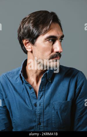 Confident young male in blue shirt on gray background and looking away Stock Photo