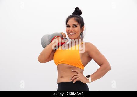Low angle of positive fit woman in orange top standing with hand on waist against gray cloudy sky with heavy weight looking at camera Stock Photo