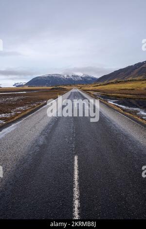 Perspective view of empty asphalt road going through field with dry grass against cloudy sky in Vik, Iceland Stock Photo