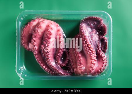 Top view of raw pink octopus placed in plastic box on green background Stock Photo