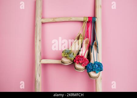 Multicolored sandals decorated with flowers hanging on wooden ladder placed near bright pink wall Stock Photo