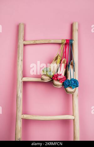 Multicolored sandals decorated with flowers hanging on wooden ladder placed near bright pink wall Stock Photo