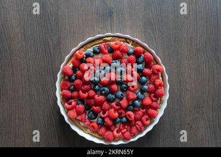 Delicious home made raspberry and blueberry mixed fruit pastry tart dessert in a white ceramic dish on a kitchen worktop Stock Photo