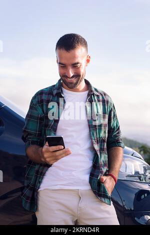 man using mobile phone leaning on his camper van Stock Photo