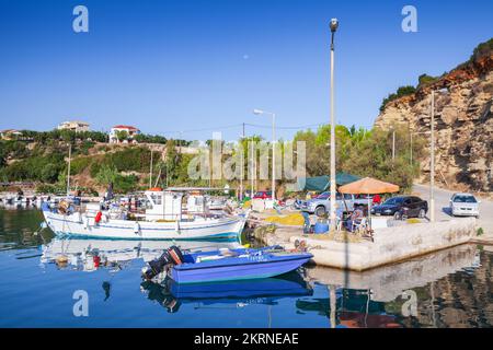 Zakynthos, Greece - August 21, 2016: Fishing boats are moored in Tsilivi on a sunny day. Fishermen sit under umbrella on the pier Stock Photo