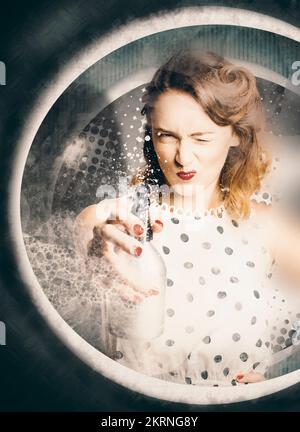 Funny retro photo of a perfect 50s style housewife pointing and shooting detergent outside washing machine window with laundry liquid stain remover. C Stock Photo