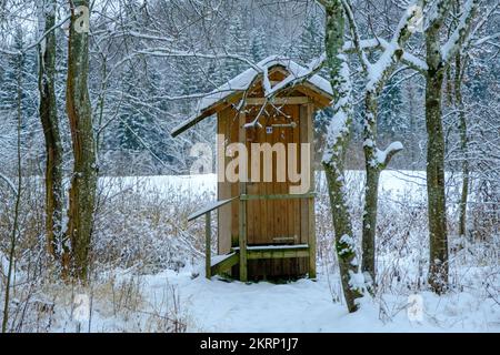 Outdoor wooden toilet house covered with snow on winter forest and trees background. Among the trees by the tourist trail. Stock Photo