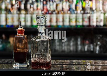 decanters with angostura and sweet liqueur stand in the semi-darkness on the bar counter of a nightclub. Ingredients for making cocktails. Stock Photo