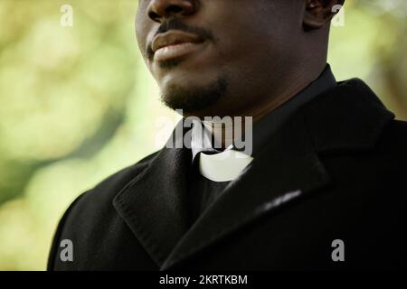 Close up of African American priest wearing black at outdoor funeral ceremony with focus on clerical collar, copy space Stock Photo