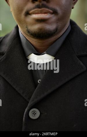 Vertical closeup of African American priest wearing black at outdoor funeral ceremony with focus on clerical collar Stock Photo