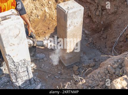 Construction worker using electric jackhammer drill to break reinforced concrete pillar in building site. Stock Photo