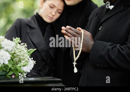 Close up of people wearing black at outdoor funeral ceremony with focus on hands in prayer holding rosary Stock Photo